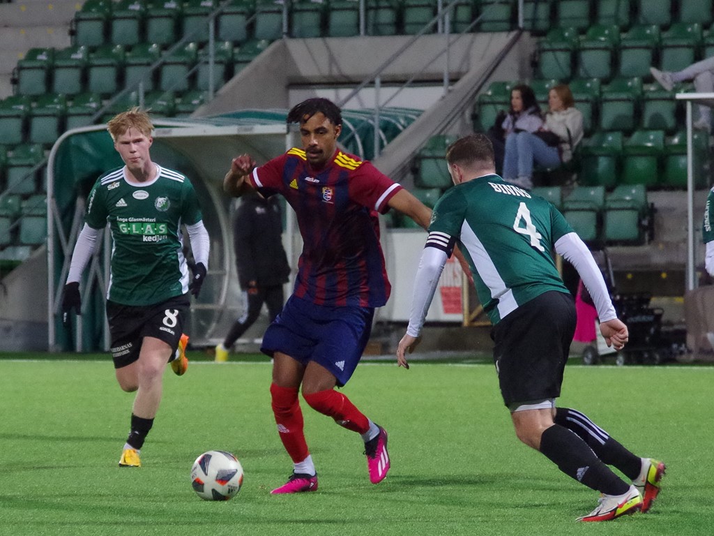 SSK:s Senay Haile Gaim funderar på nästa drag, Östavalls lagkapten Jordan Binns är beredd. I bakgrunden en riktig Wiking. Foto: Pia Skogman, Lokalfotbollen.nu.